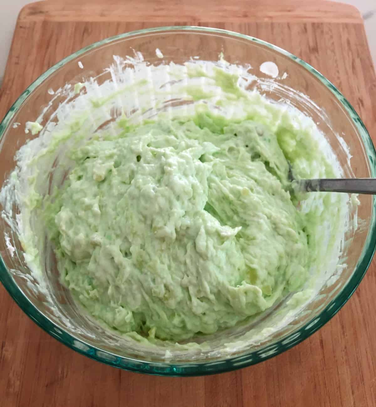Mixing Watergate salad in glass bowl with spoon.