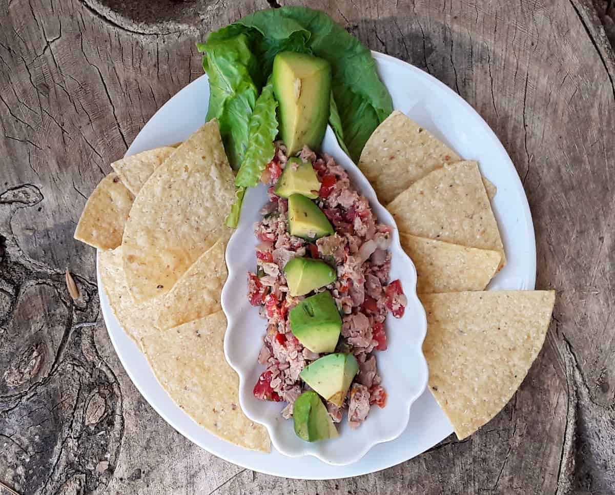 Tuna ceviche topped with avocado chunks on plate with baked tortilla chips.