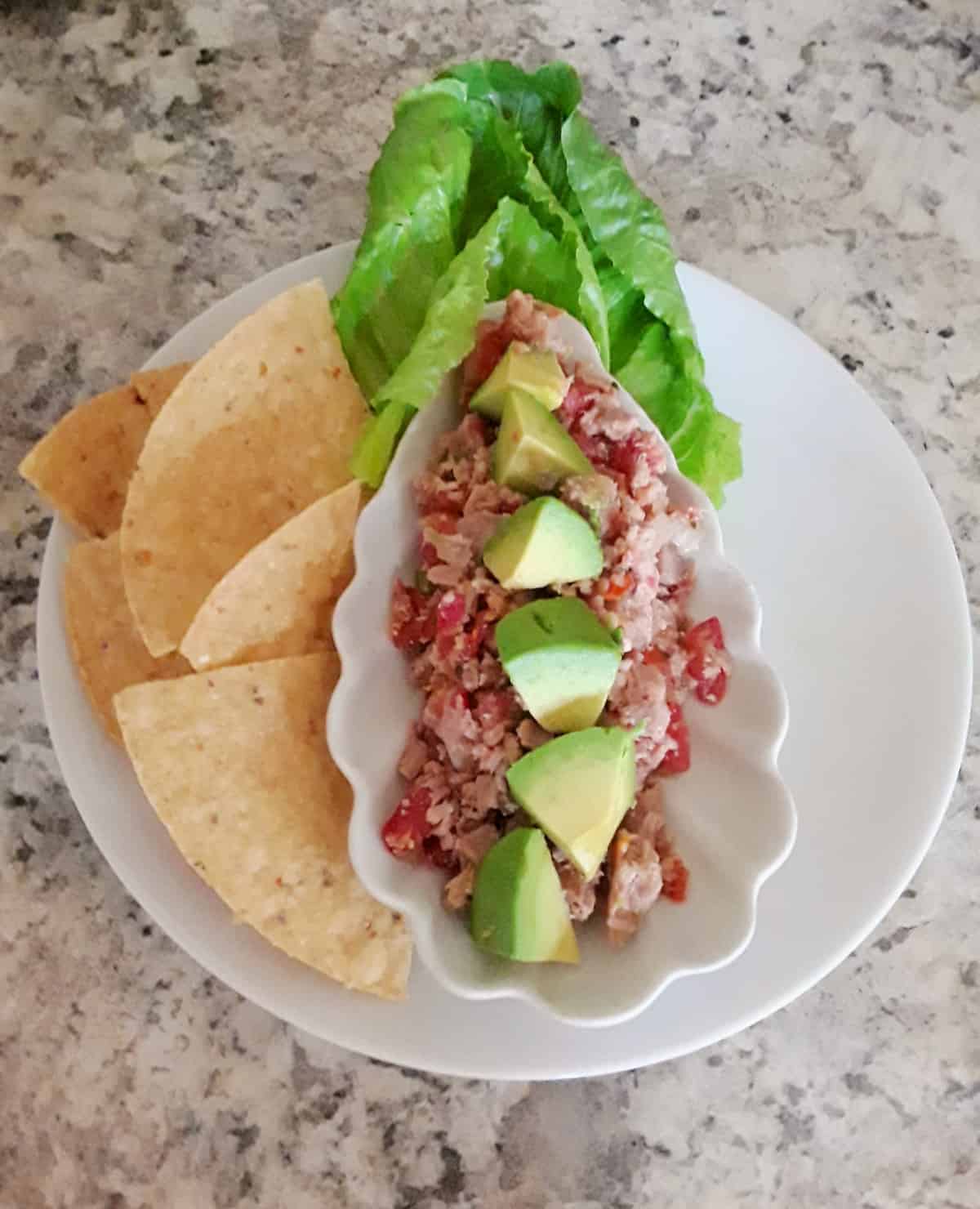 Tuna ceviche garnished with chopped avocado on white platter with lettuce and chips.
