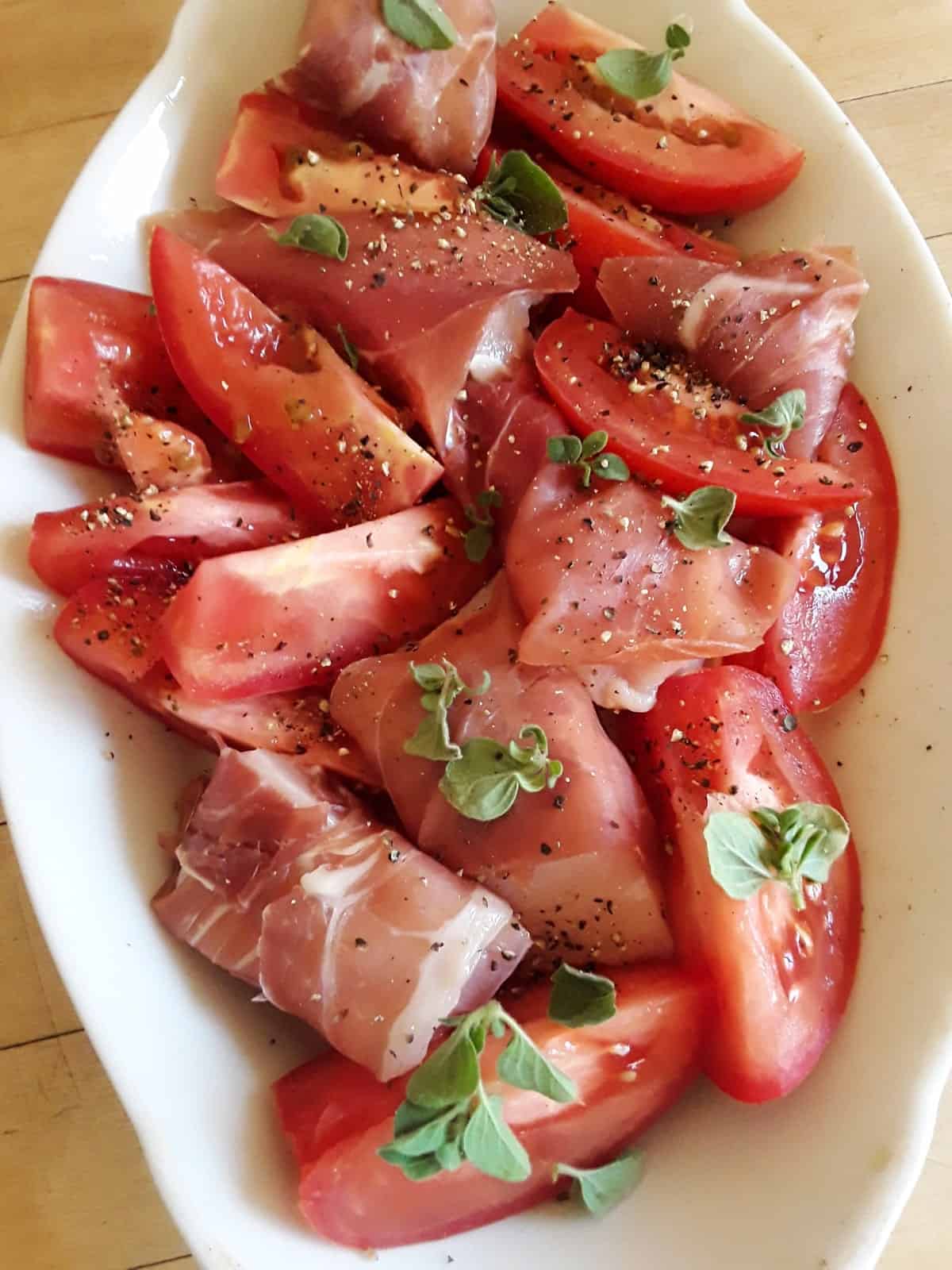Uncooked prosciutto wrapped chicken with tomatoes and oregano in baking dish