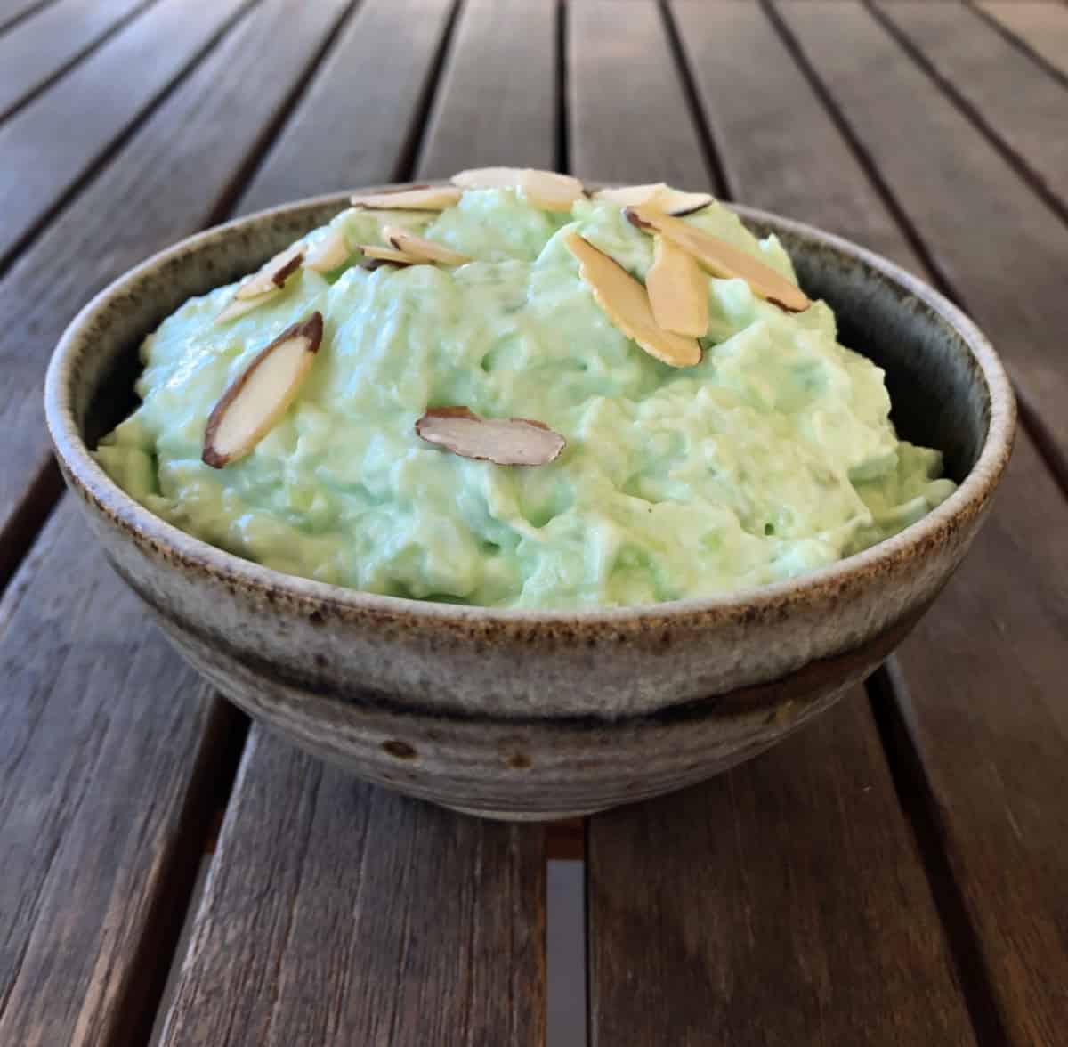 Watergate pistachio jello salad topped with sliced almonds in ceramic bowl.