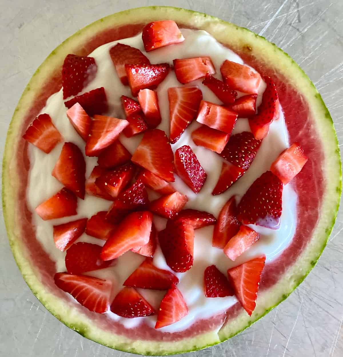 Watermelon slice topped with yogurt and fresh strawberries.