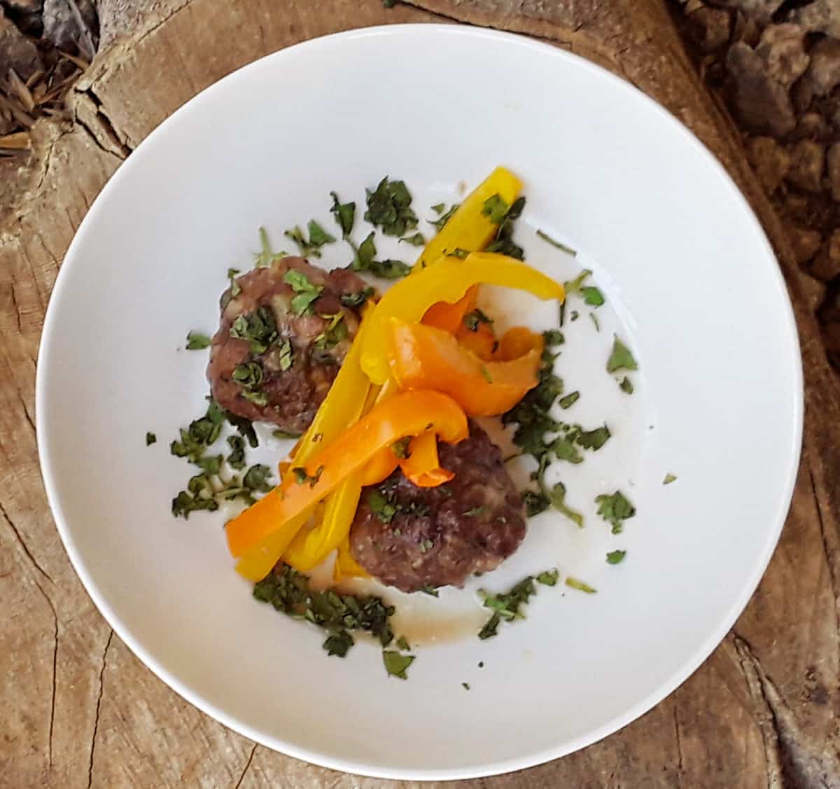 Baked meatballs with peppers on white dinner plate garnished with fresh chopped herbs.