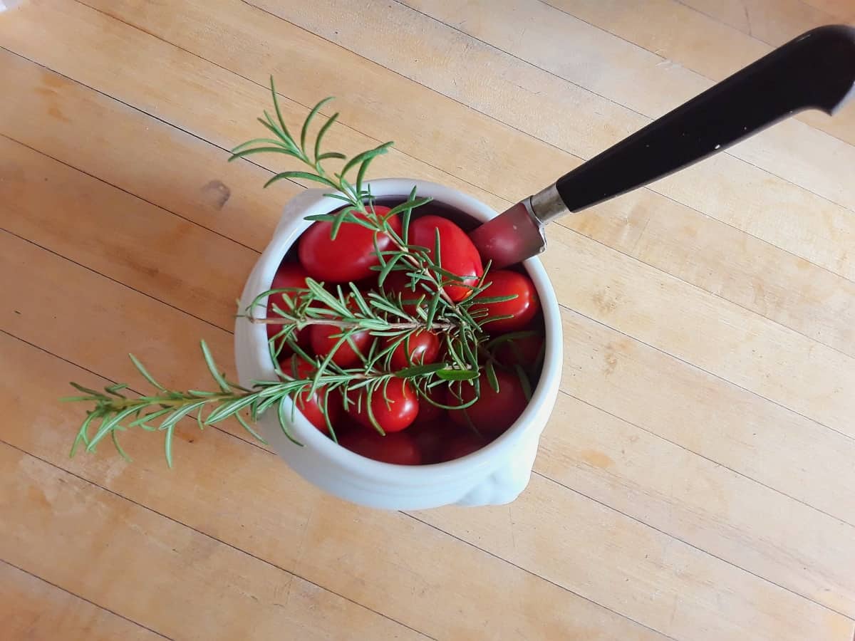 Cherry tomatoes in small white bowl with fresh rosemary and knife.