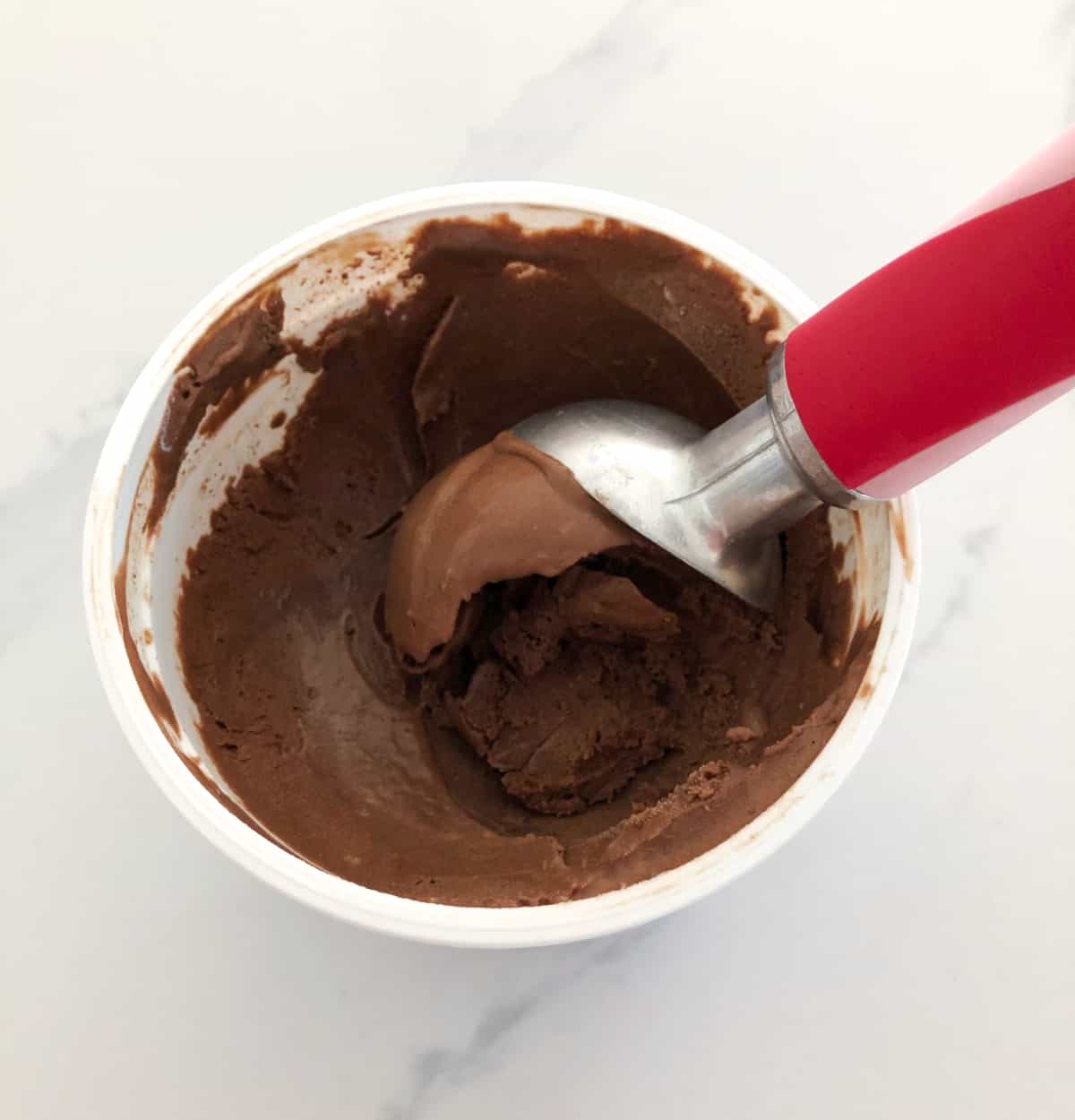 Scooping chocolate gelato with red handled ice cream scoop.