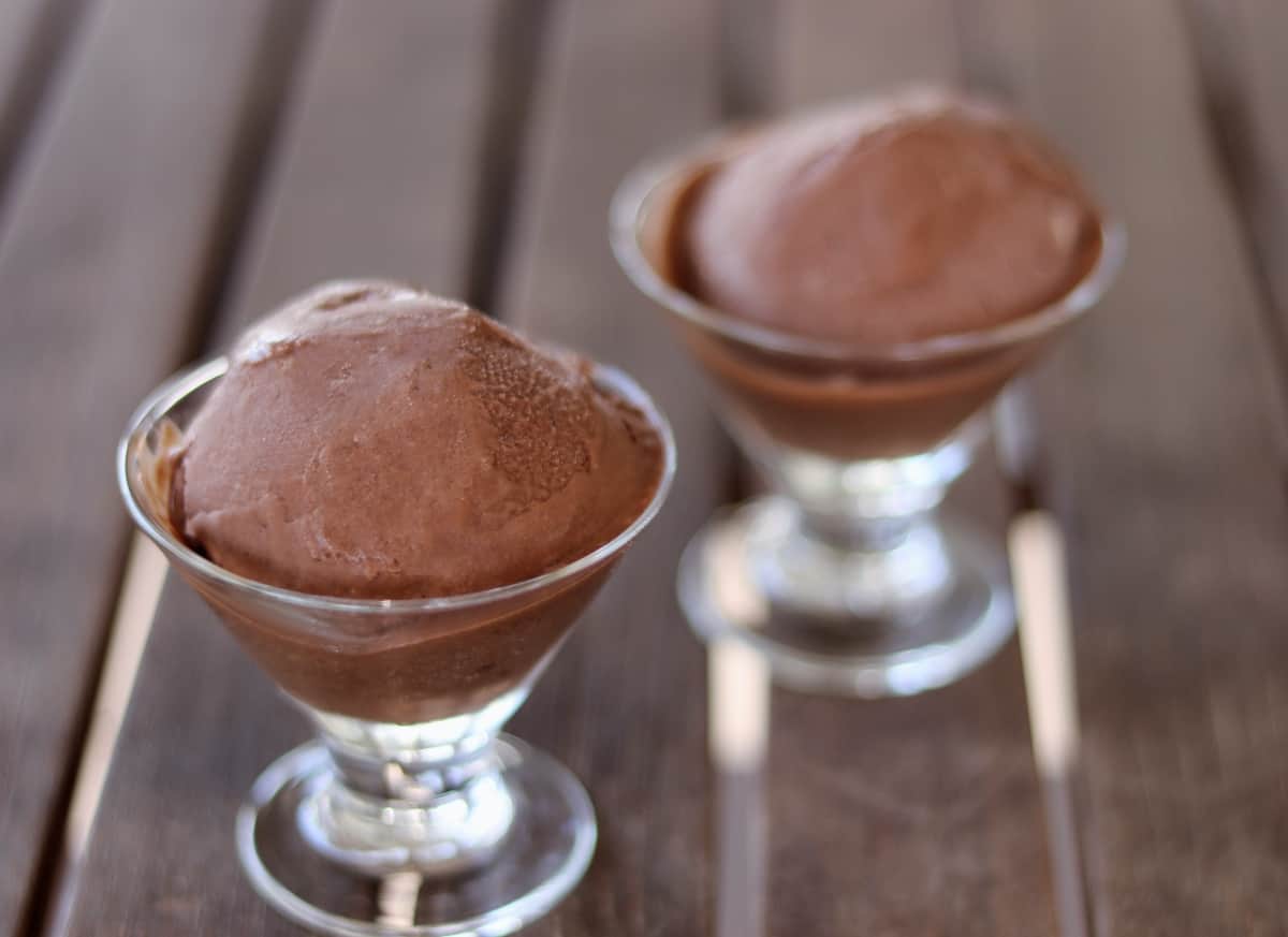 Two stemmed dessert glasses with chocolate gelato on wooden table.