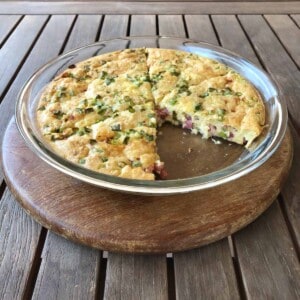 glass pie plate with ham and swiss pie set on wooden cutting board