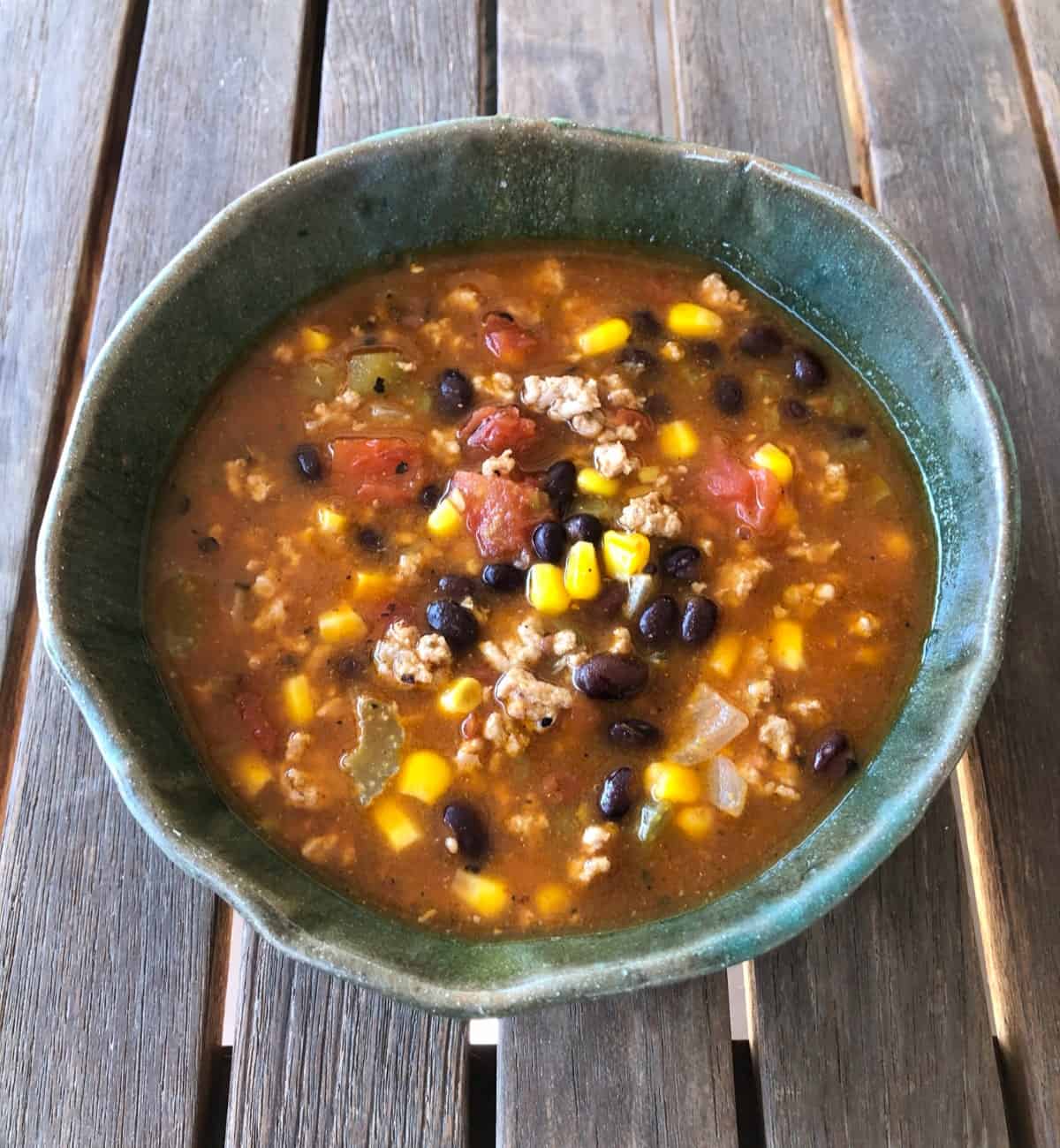 Instant pot turkey taco soup in green ceramic bowl on wooden table.