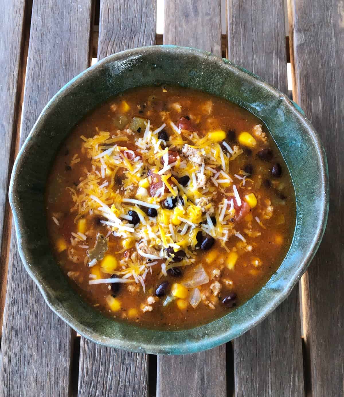 Turkey taco soup garnished with shredded cheese in green ceramic bowl.