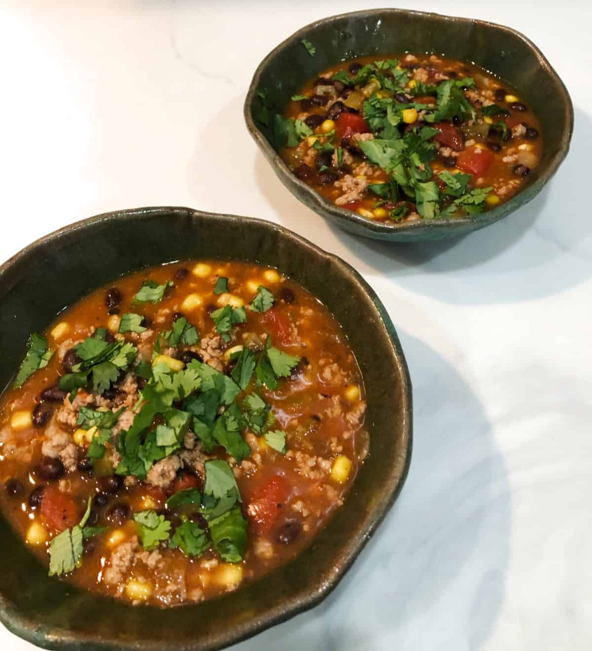 Two bowls of turkey taco soup garnished with chopped fresh cilantro.