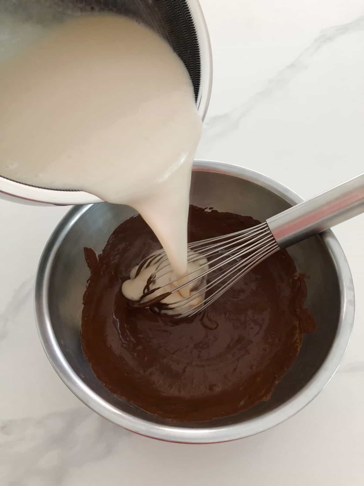Pouring warm coconut milk and cornstarch mixture into chocolate mixture.