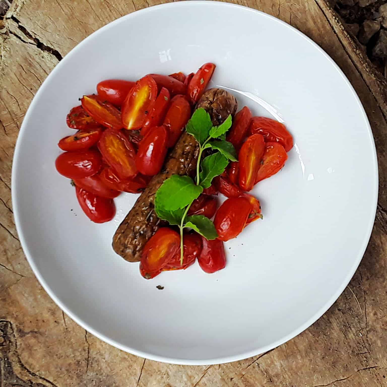 Spicy sausages with tomatoes on white plate garnished with fresh basil.