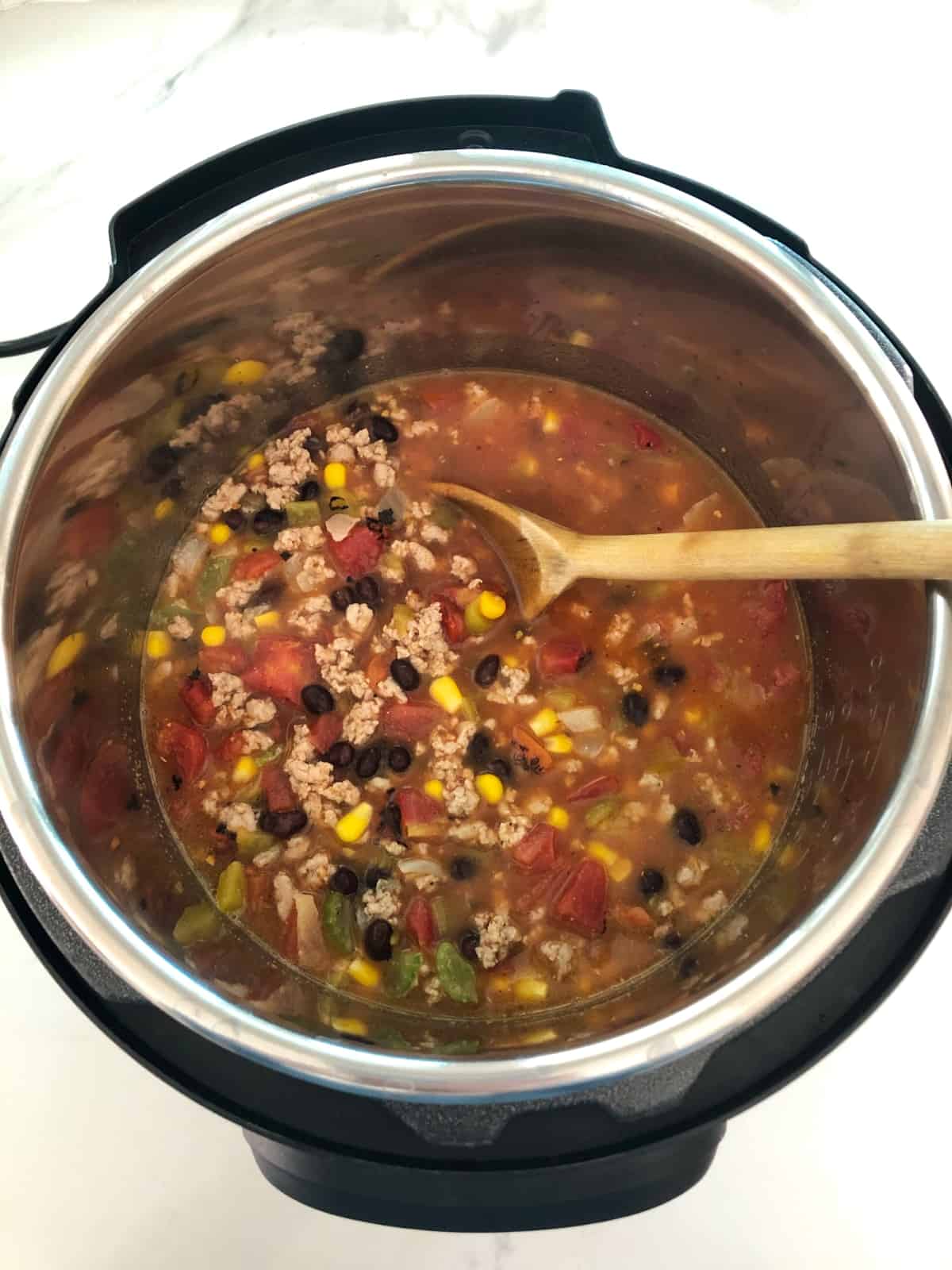 Instant Pot with uncooked turkey taco soup and wooden spoon.