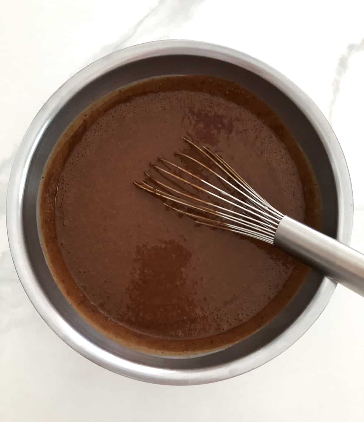 Unfrozen chocolate gelato in mixing bowl with whisk.