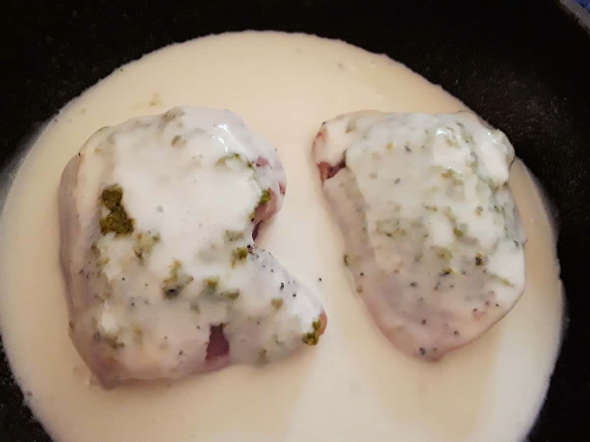 Chicken thighs in coconut milk topped with pesto in baking dish.