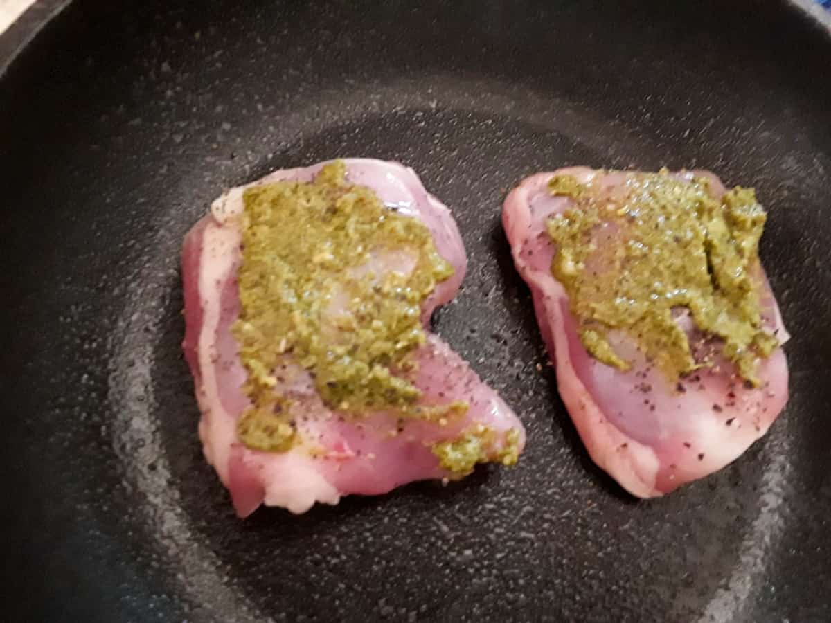 Chicken thighs topped with pesto in baking pan.
