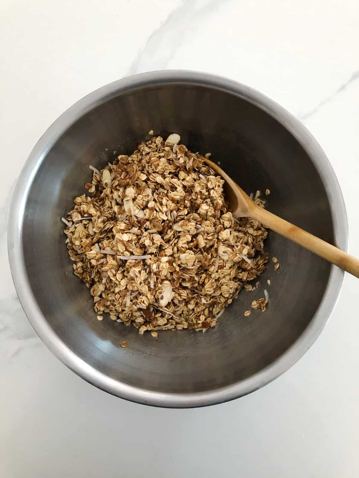Stirring almond granola in mixing bowl with wooden spoon.