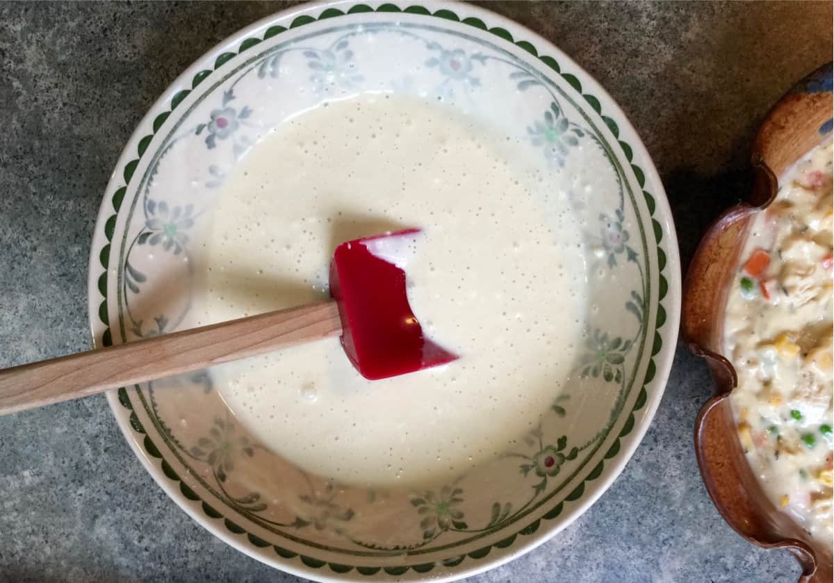 Mixing milk, egg and baking mix in bowl with red spatula.