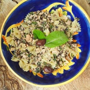 Tuna pasta salad with olive tapenade garnished with fresh basil in a colorful blue bowl