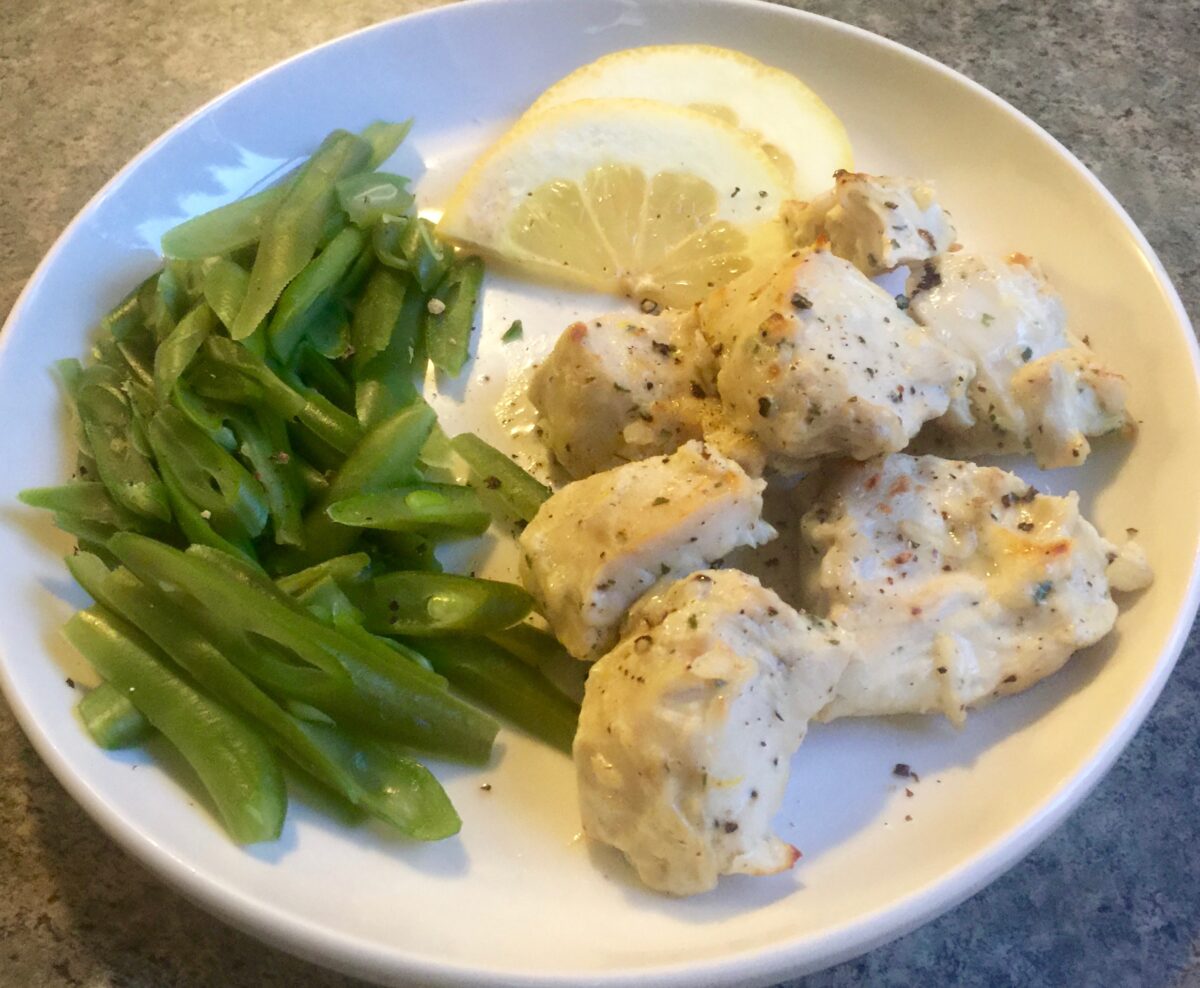 Creamy Ranch Chicken Bites with lemon wedges and green beans on white dinner plate.