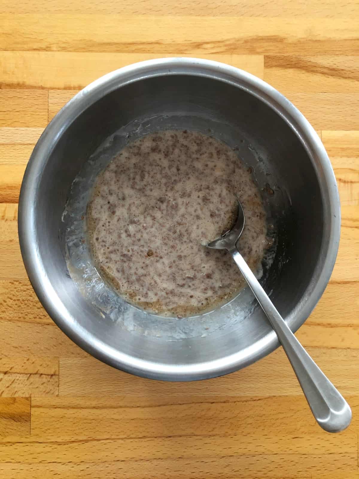 Mixing batter in stainless steel bowl with spoon for making blueberry bran muffin tops.