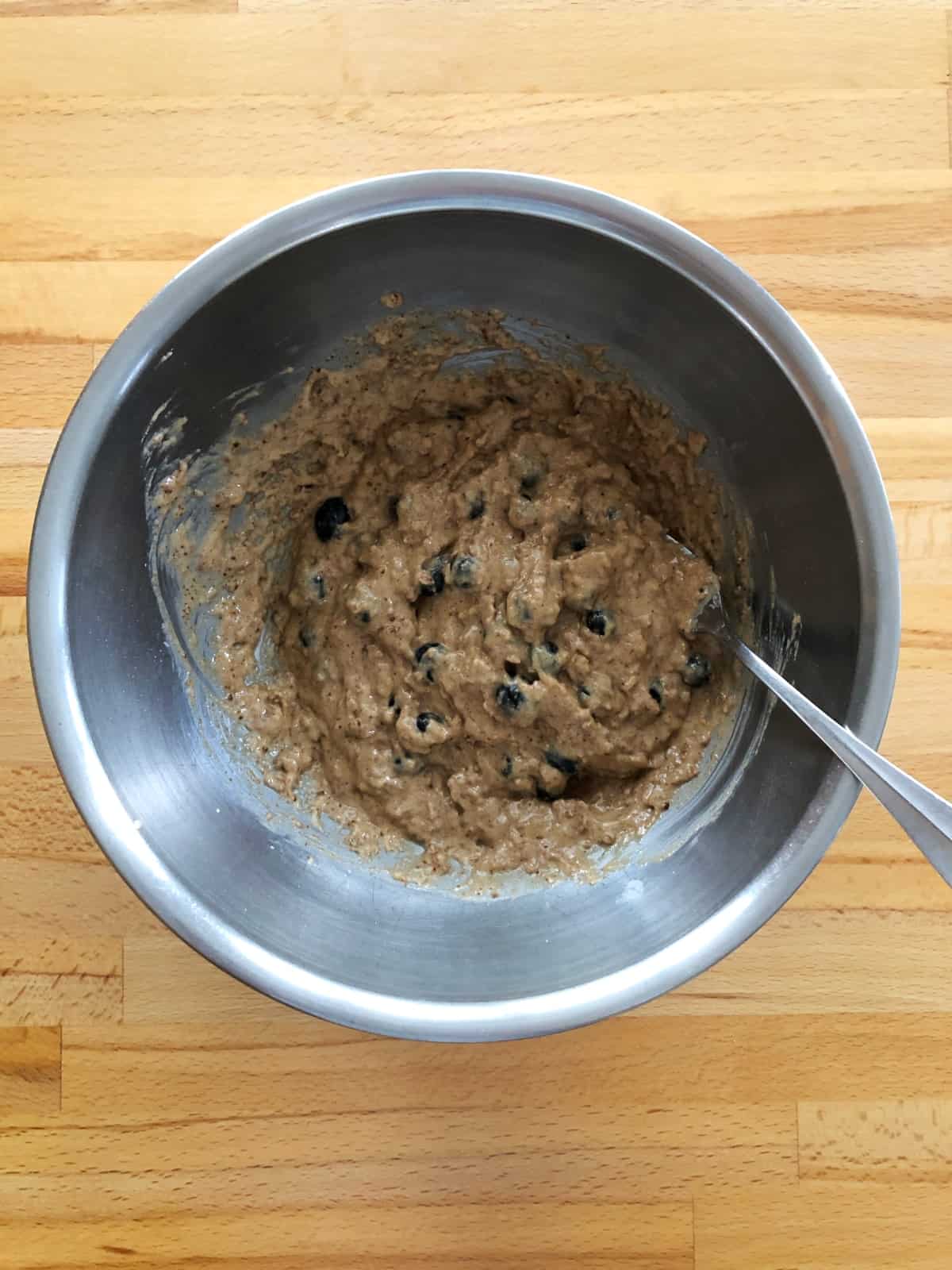 Folding fresh blueberries into bran muffin top batter in stainless mixing bowl with a fork.