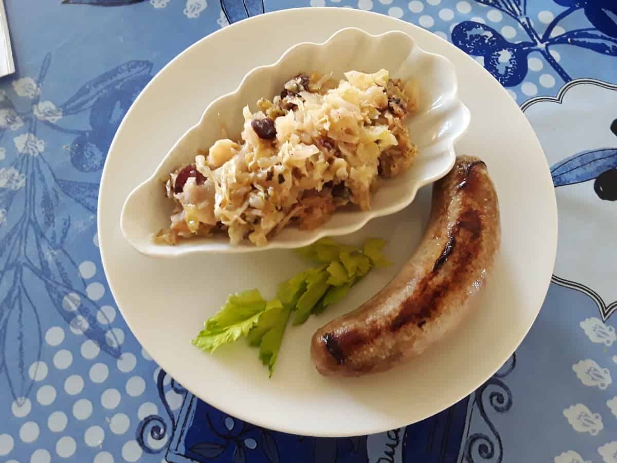 Grilled sausage on white plate with braised cabbage and craisins in small white dish.