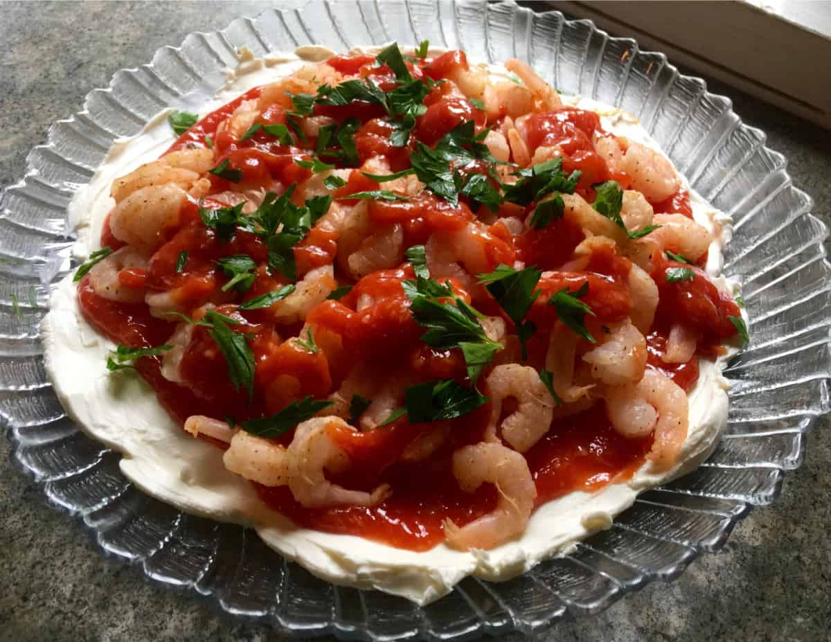 Cream cheese shrimp dip garnished with fresh parsley in glass serving dish.