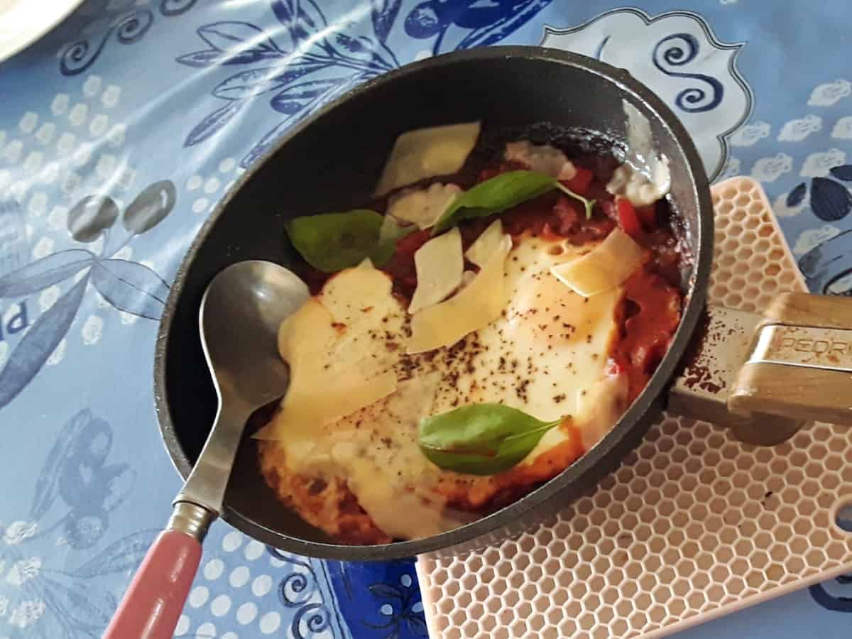 Marinara baked eggs in skillet with shaved parmesan and basil leaves.