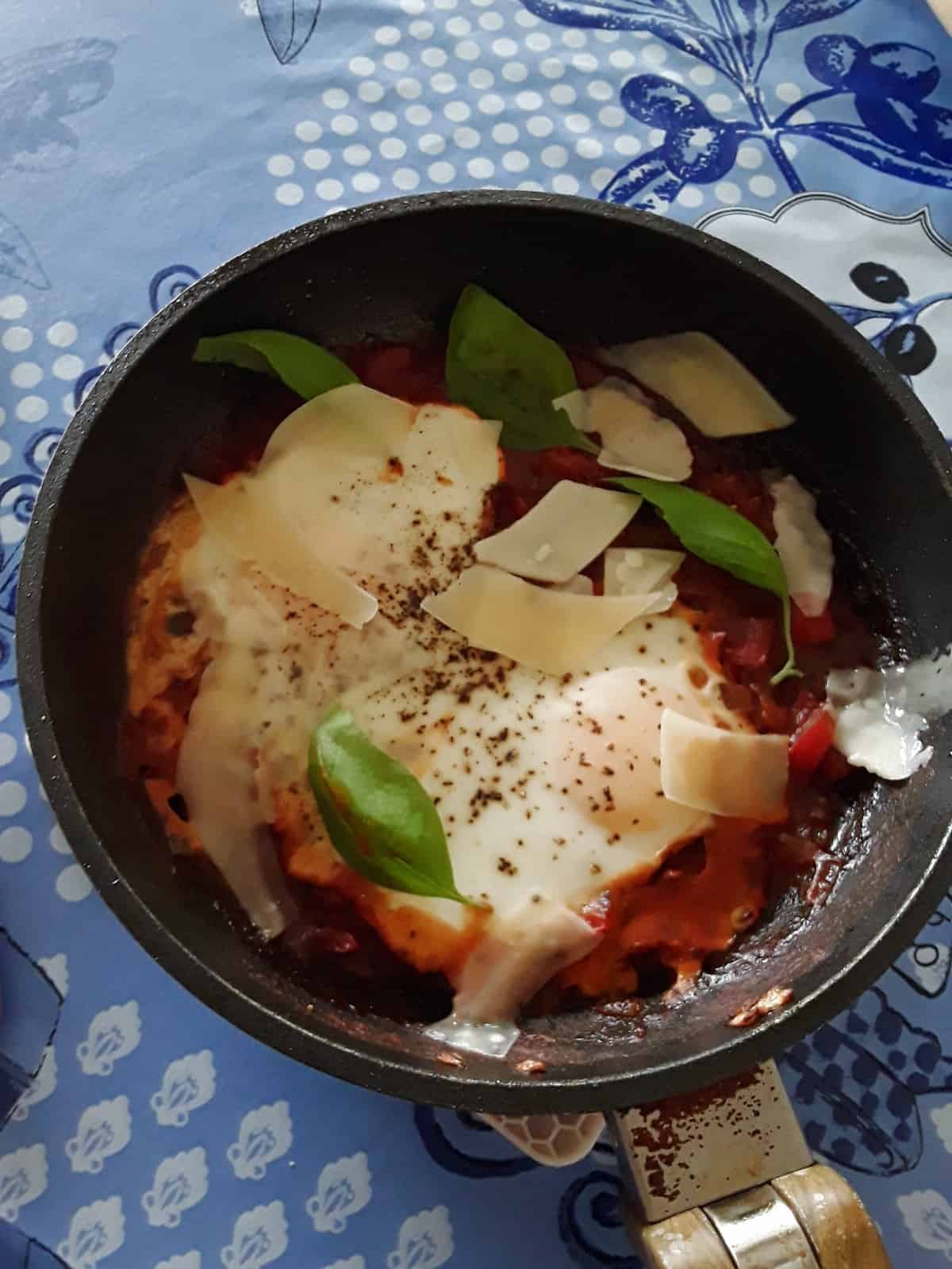 Marinara Baked Eggs in skillet topped with shaved Parmesan cheese and fresh basil.