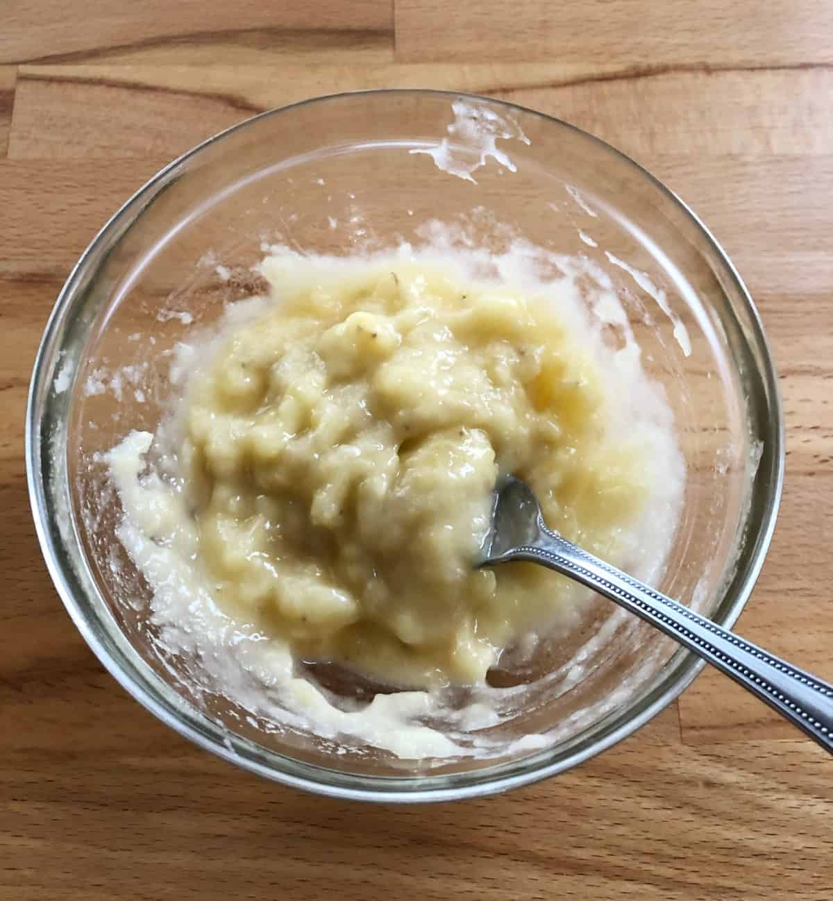 Mashed overripe banana in glass bowl with fork.