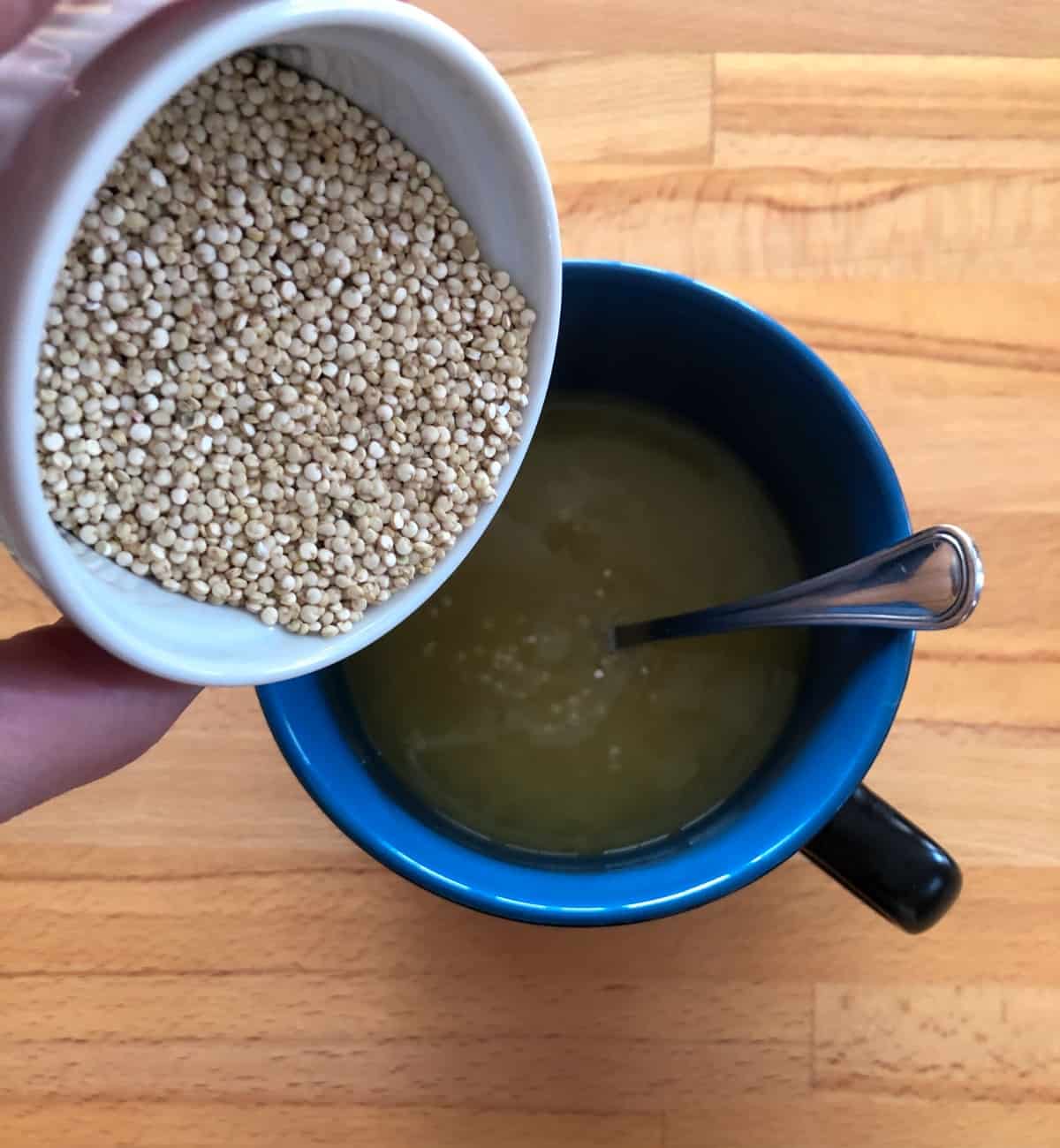 Pouring dry quinoa into mug filled with chicken broth.