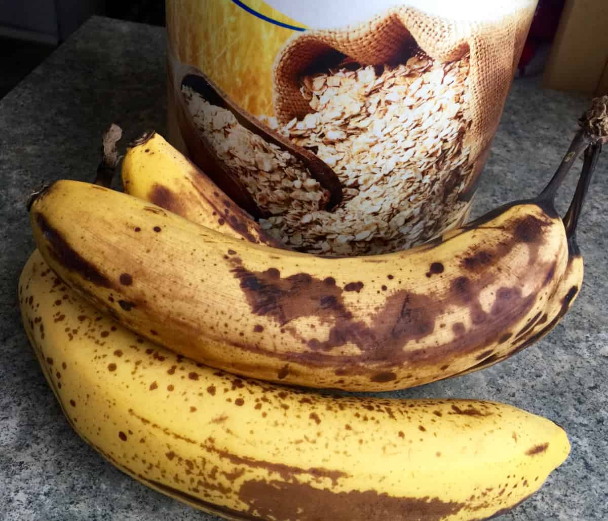 Container of rolled oats and ripe bananas up close.