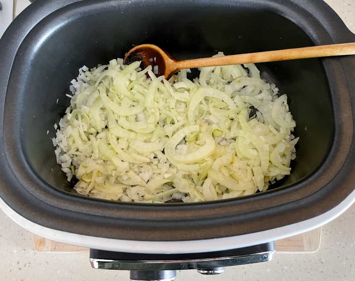 Cooking onions and fennel in multi-cooker with wooden spoon.