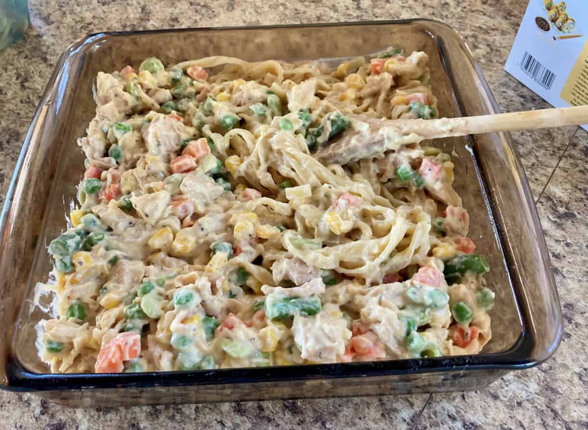 Stirring together chicken noodle casserole ingredients in pyrex casserole dish.