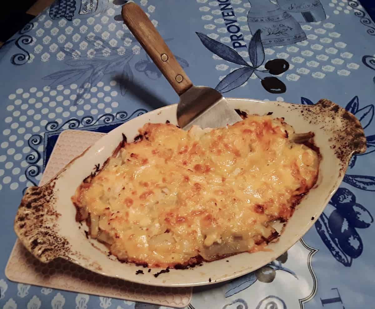 Cheesy potato bacon bake in casserole dish with serving spoon.