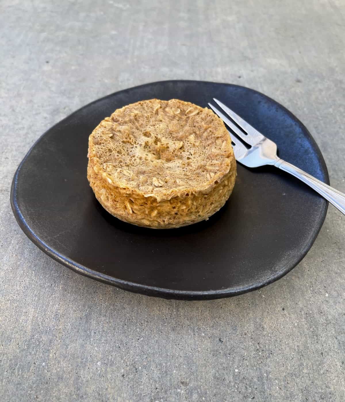 Fresh made oatmeal raisin mug muffin on brown pottery plate with fork.