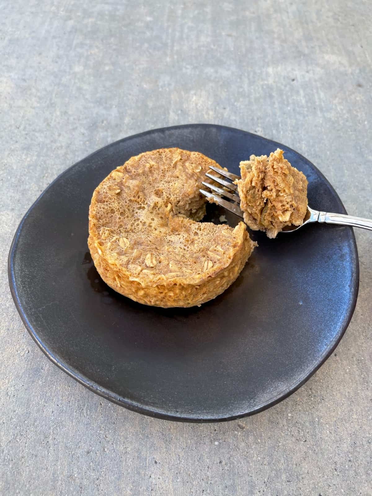 Oatmeal raisin muffin on brown plate with piece of muffin on fork.