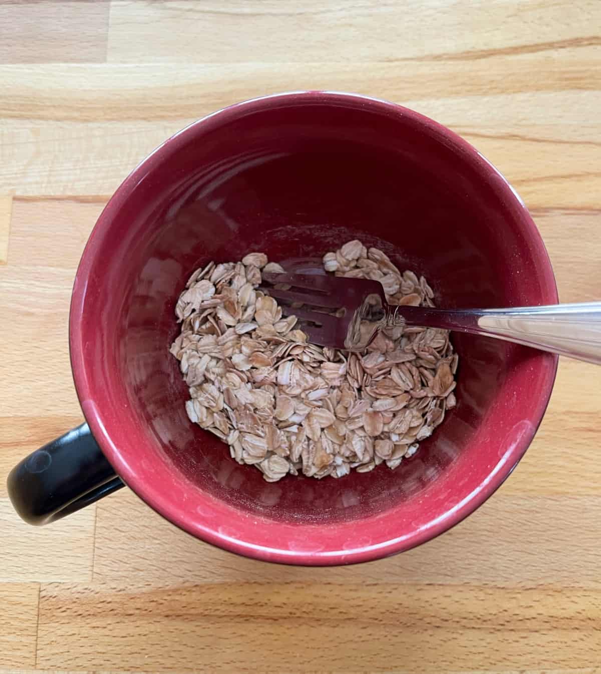 Mixing rolled oats, cinnamon and baking powder in red mug with fork.