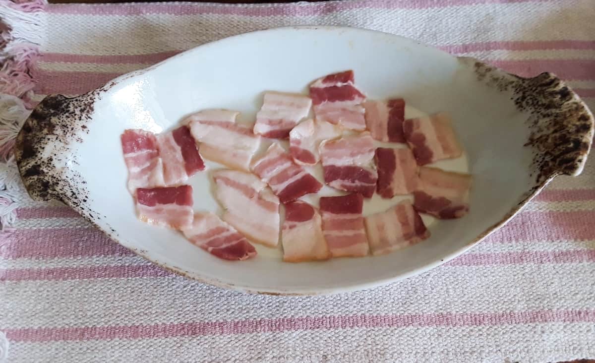 Sliced bacon layered in bottom of small casserole dish.