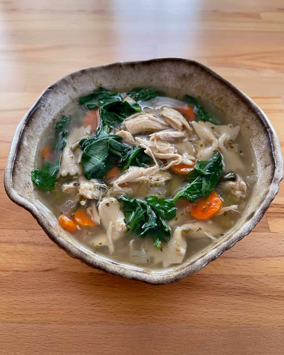 Tuscan chicken pasta soup in ceramic bowl on wooden table.