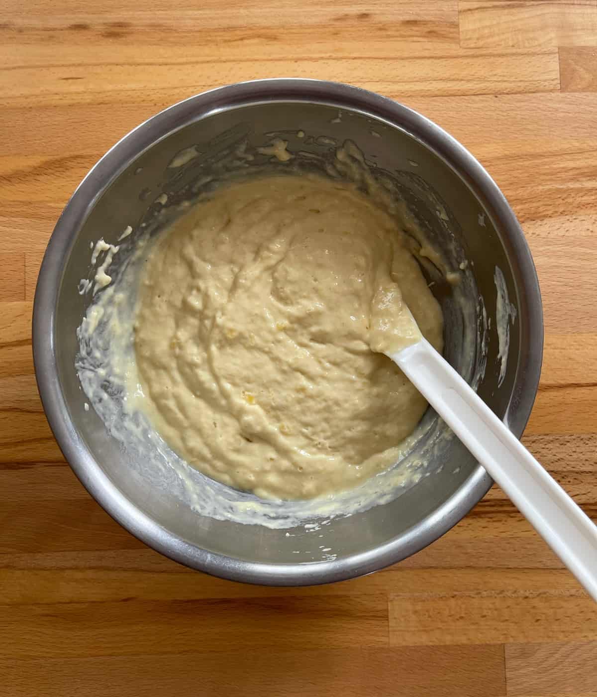 Mixing skillet pancake batter in mixing bowl with spatula on wooden table.