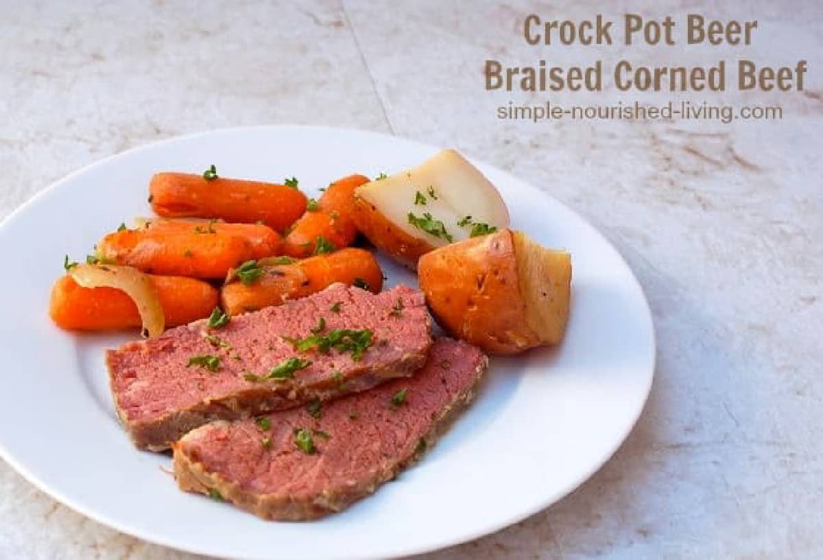 Sliced beer-braised corned beef on white plate with potatoes and carrots.