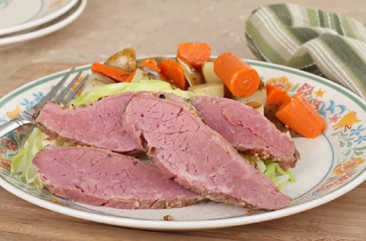Sliced of corned beef on dinner plate with carrots, potatoes and cabbage.