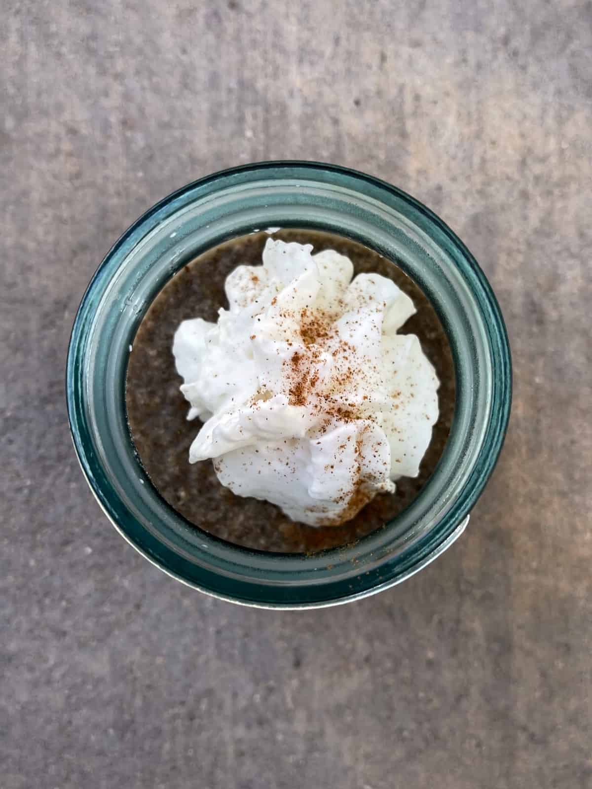 Cappuccino chia seed pudding in Mason jar with whipped cream and cinnamon sprinkle from above.