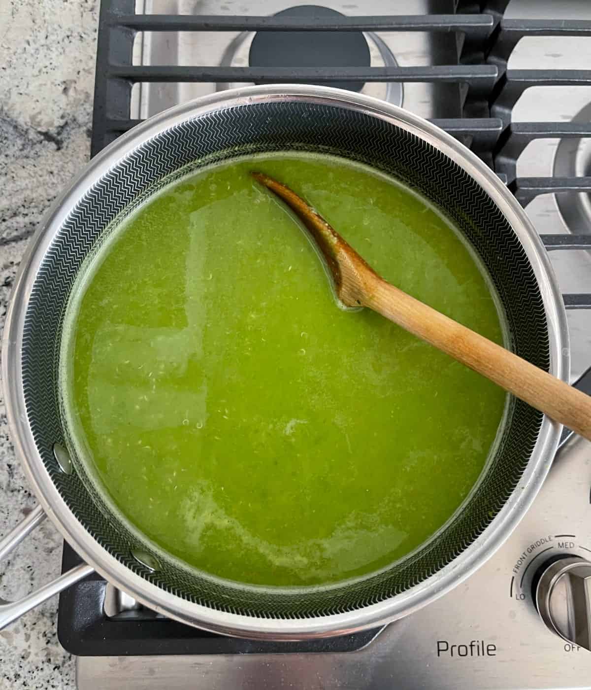 Stirring pea soup with quinoa in saucepan with wooden spoon.