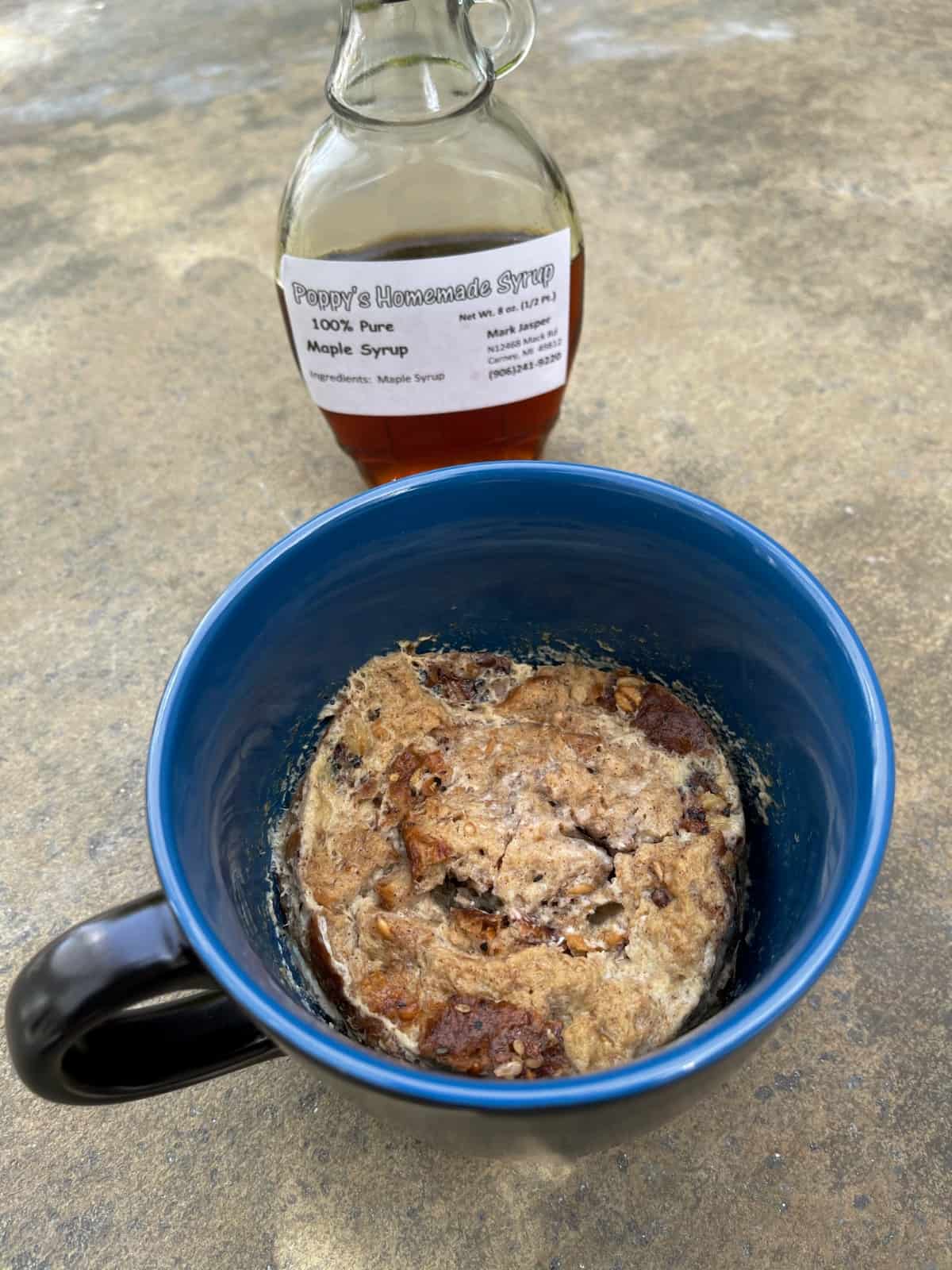 Microwave French toast in blue mug with bottle of maple syrup.