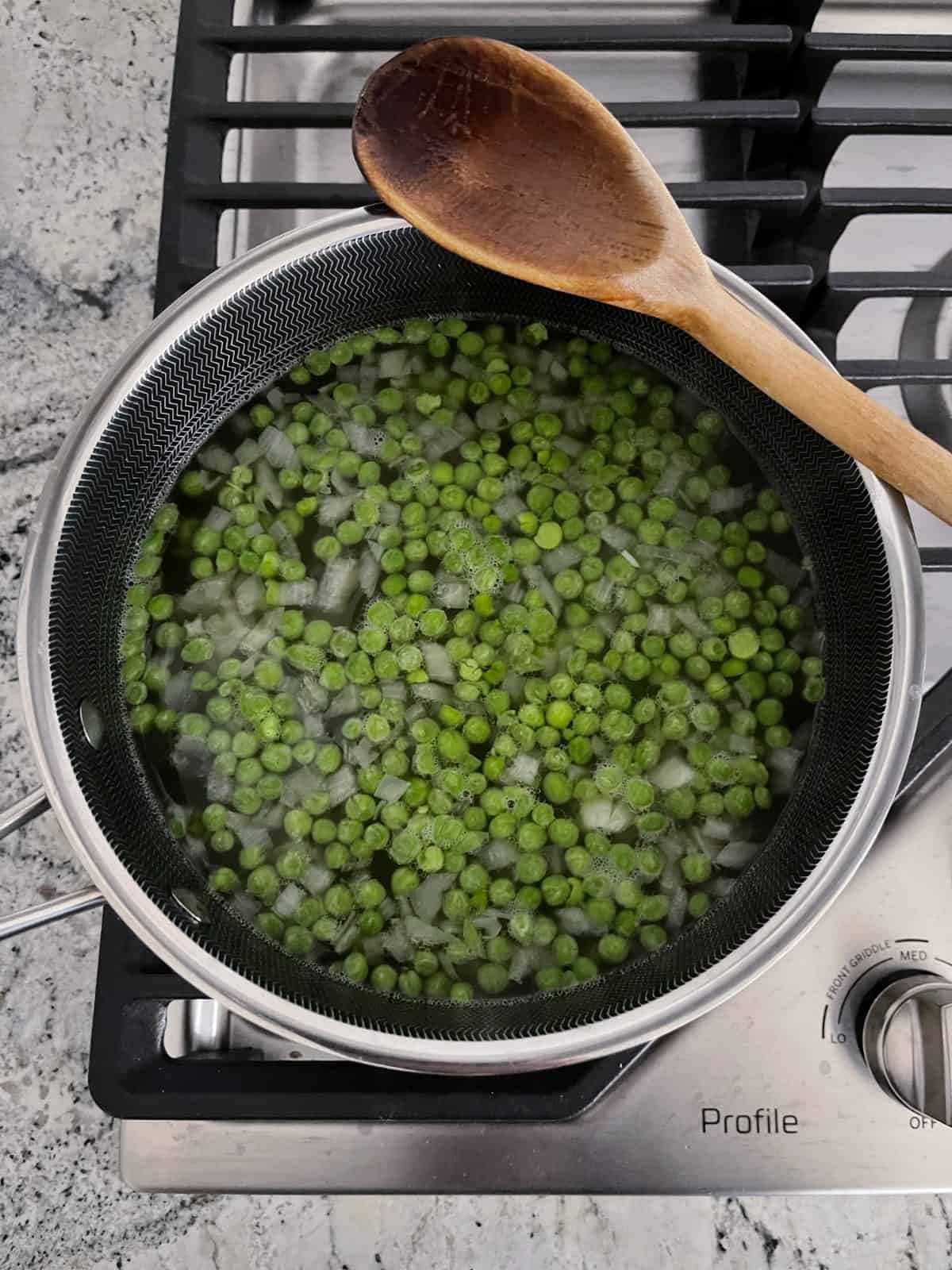 Cooking peas, chicken broth and onions in saucepan on stovetop