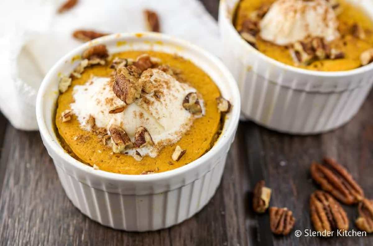 Microwave pumpkin custard dessert in small white ramekin toped with whipped topping and chopped pecans.