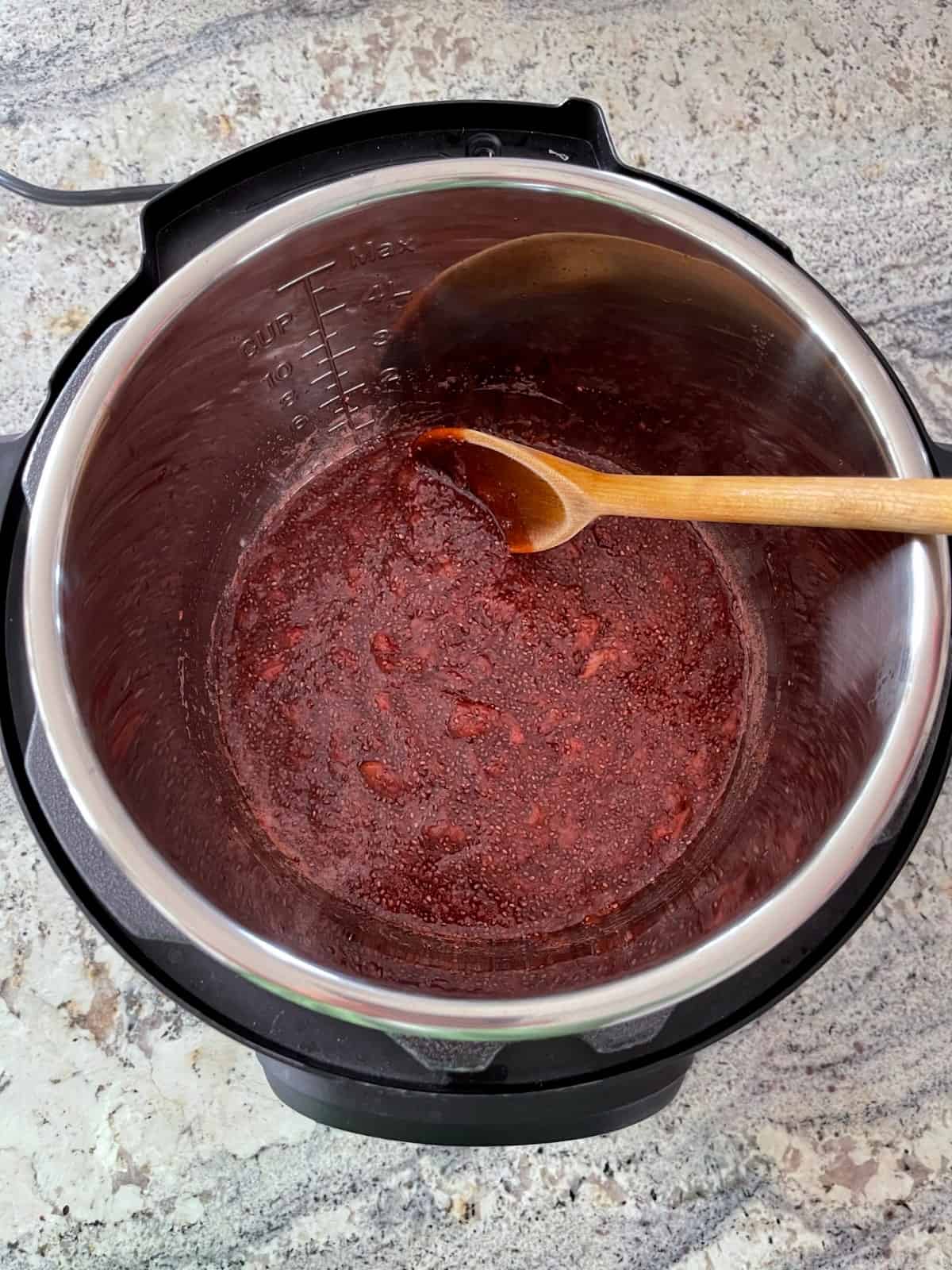 Stirring strawberry chia jam with wooden spoon in Instant Pot